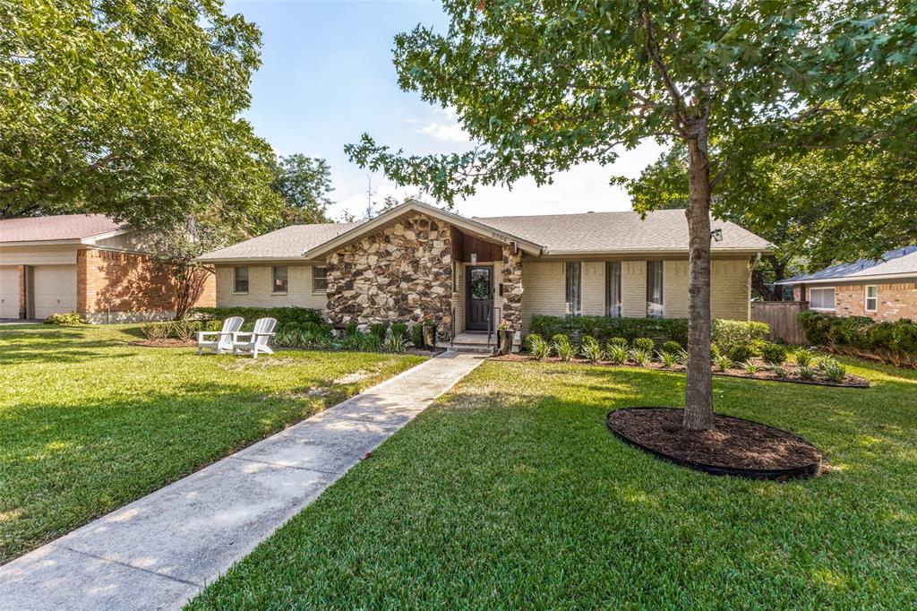 Stone facade with a covered entry, established landscaping, and a concrete pathway leading to the front door