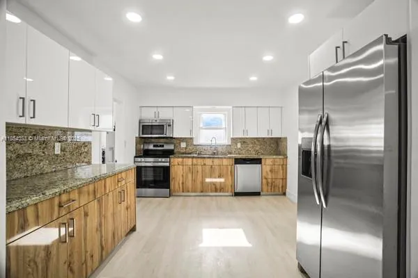 a kitchen with stainless steel appliances granite countertop a refrigerator a sink a stove top oven and cabinets