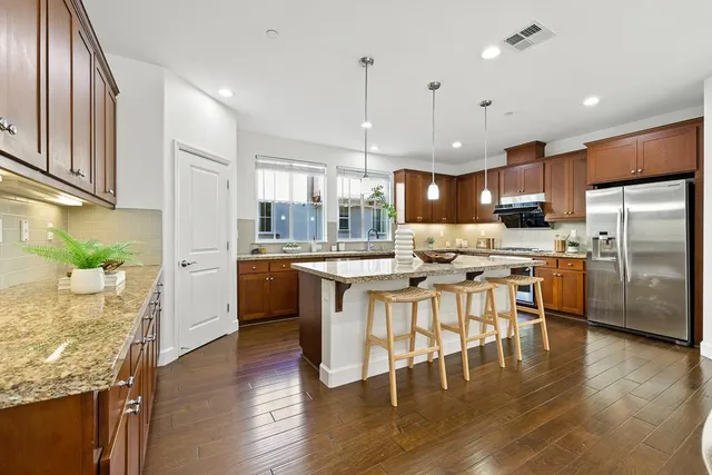 a kitchen with stainless steel appliances kitchen island granite countertop a refrigerator a sink dishwasher a stove and a dining table with wooden floor
