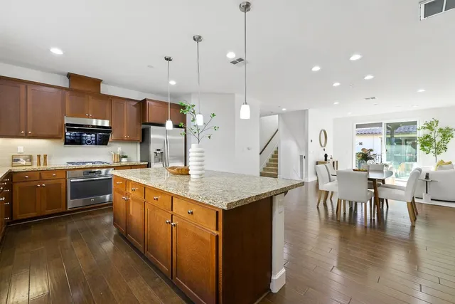 a kitchen with stainless steel appliances kitchen island granite countertop a stove top oven a sink a dining table and chairs with wooden floor
