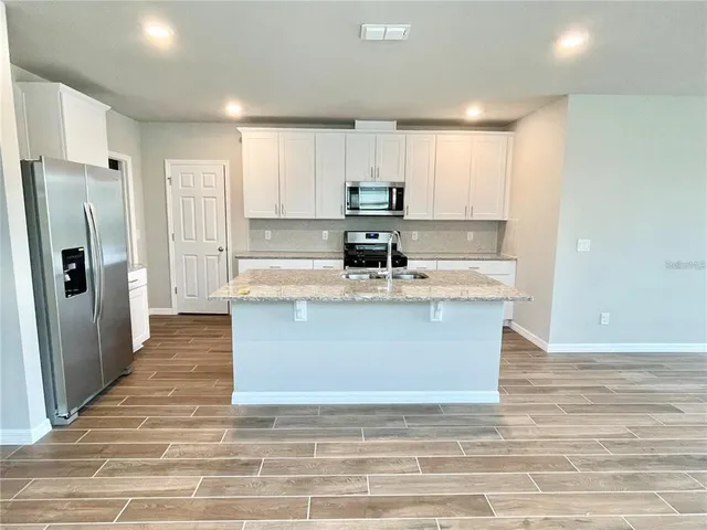 a large kitchen with stainless steel appliances granite countertop a stove a refrigerator a sink and white cabinets with a dining table