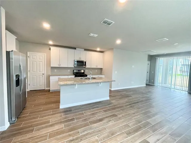 a kitchen with stainless steel appliances kitchen island granite countertop a stove a refrigerator and white cabinets with wooden floor