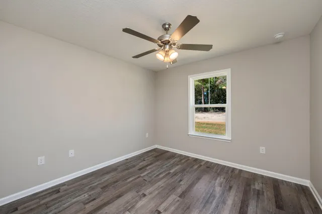an empty room with wooden floor fan and windows