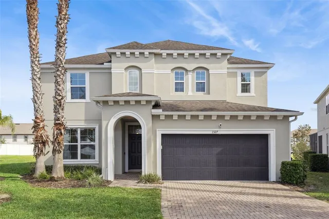 a view of a grey house with a small yard and large tree