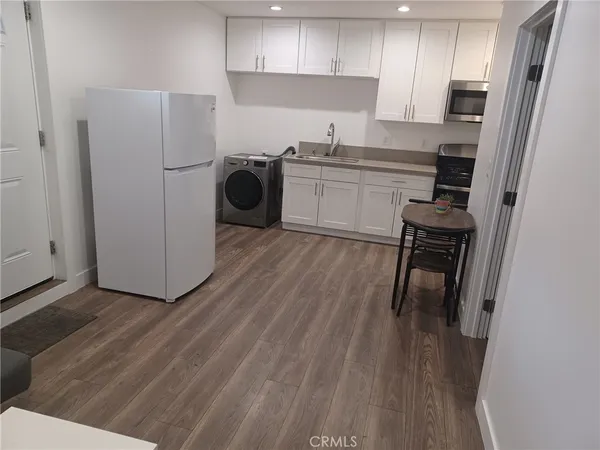 a kitchen with stainless steel appliances granite countertop a refrigerator a stove a sink and white cabinets with wooden floor