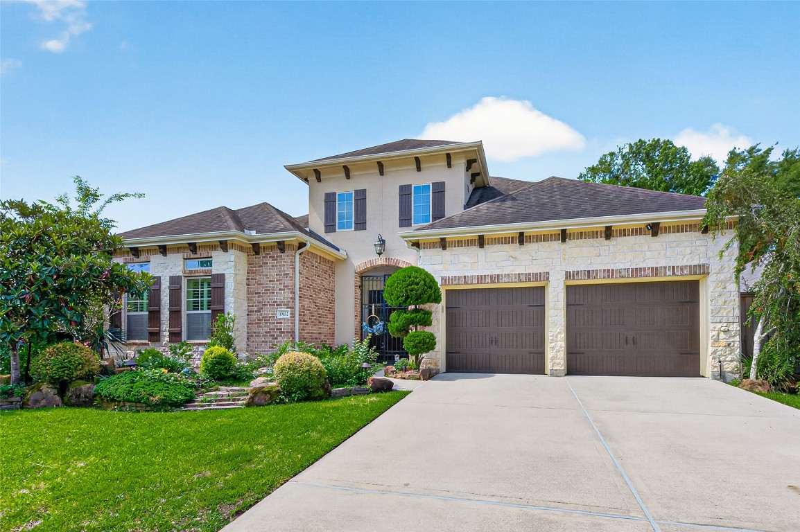 Luxury One Story Home with a spacious driveway leading to a three-car garage. The entryway is inviting, accented by tasteful landscaping and elegant shutters.