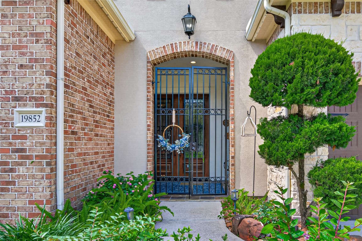 19852 Cullen Ridge Drive Porter, TX 77365 - Photo 9 of 43 Charming entrance with a wrought iron gate, brick accents, and a welcoming wreath. Lush greenery and decorative plants enhance the inviting curb appeal.