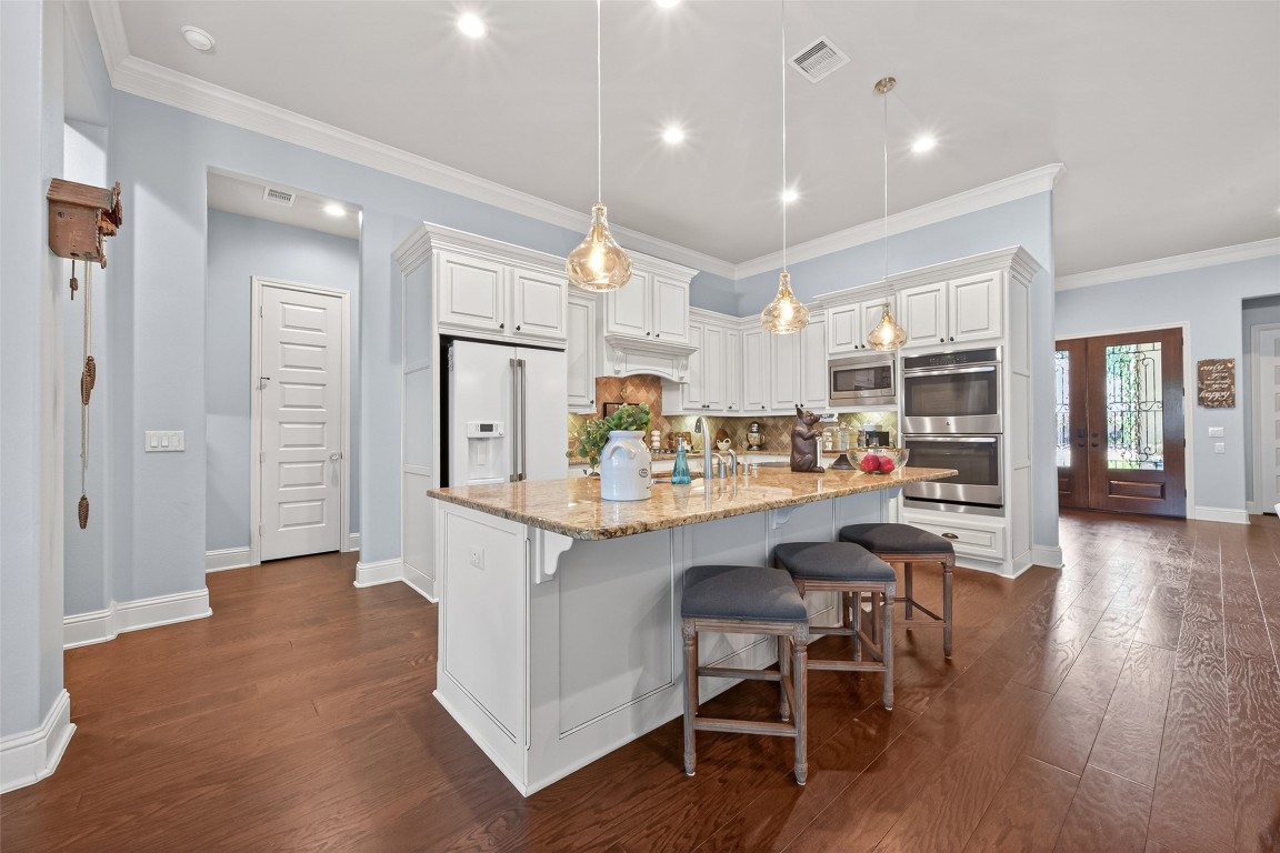 19852 Cullen Ridge Drive Porter, TX 77365 - Photo 16 of 43 Modern kitchen with elegant white cabinetry, granite countertops, and stainless steel appliances. It features an island with seating, pendant lighting, and hardwood floors, providing a warm, inviting ambiance.