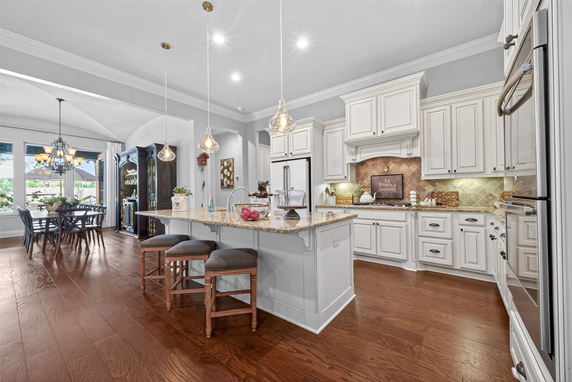 19852 Cullen Ridge Drive Porter, TX 77365 - Photo 41 of 43 This spacious kitchen features elegant white cabinetry, a large central island with bar seating, and stylish pendant lighting. The open floor plan connects to a bright dining area with large windows and hardwood floors, creating a warm and inviting space for entertaining.