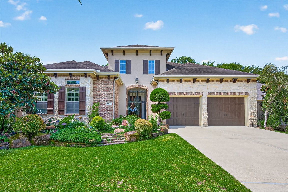 19852 Cullen Ridge Drive Porter, TX 77365 - Photo 6 of 43 Luxury One Story Home features brick and stone exterior, dark shutters, and a three-car tandem garage. The well-maintained front yard includes lush greenery and a stone pathway leading to the gated entrance, creating inviting curb appeal and privacy.