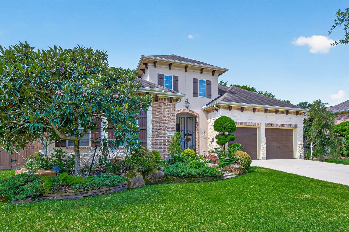 19852 Cullen Ridge Drive Porter, TX 77365 - Photo 7 of 43 Luxury One Story Home features brick and stone exterior, dark shutters, and a three-car tandem garage. The well-maintained front yard includes lush greenery and a stone pathway leading to the gated entrance, creating inviting curb appeal and privacy.