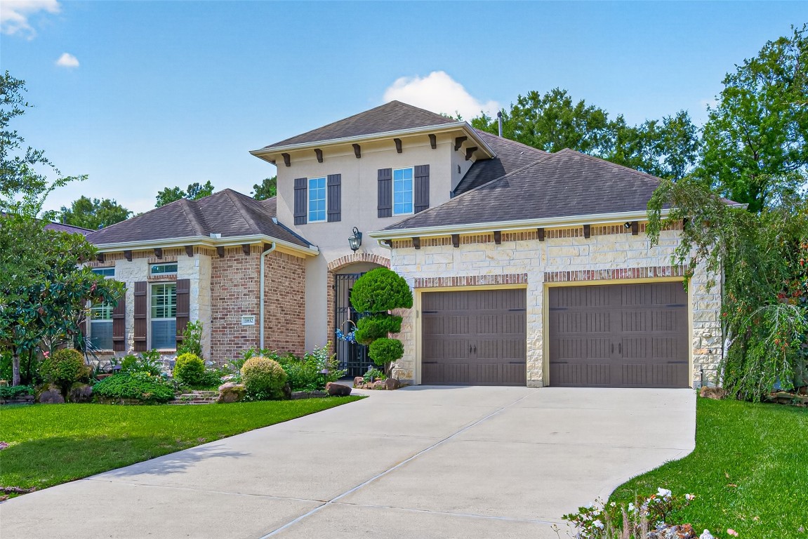 19852 Cullen Ridge Drive Porter, TX 77365 - Photo 8 of 43 Luxury One Story Home features brick and stone exterior, dark shutters, and a three-car tandem garage. The well-maintained front yard includes lush greenery and a stone pathway leading to the gated entrance, creating inviting curb appeal and privacy.