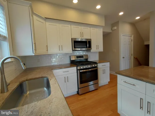 a large kitchen with stainless steel appliances kitchen island a large counter top and a wooden floors