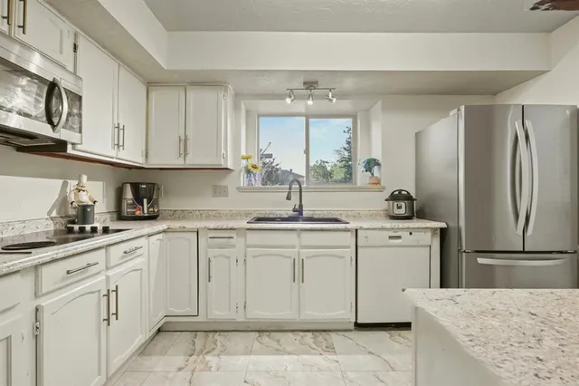 a kitchen with granite countertop white cabinets stainless steel appliances a sink and a window