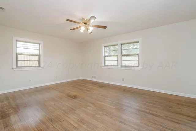 a view of an empty room with wooden floor and a ceiling fan