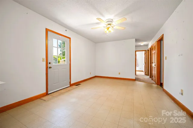 an empty room with chandelier fan and windows