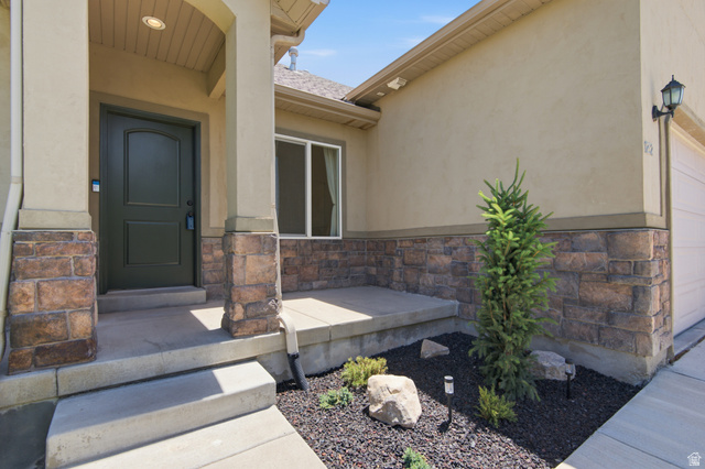 1252 Skyline Road Saratoga Springs, UT 84045 - Photo 7 of 51 Entryway featuring a dark green paneled door, stone veneer accents, stucco exterior, covered porch, and concrete steps