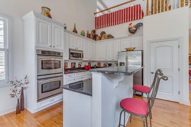 a kitchen with stainless steel appliances granite countertop a refrigerator a stove a sink dishwasher and white cabinets with wooden floor