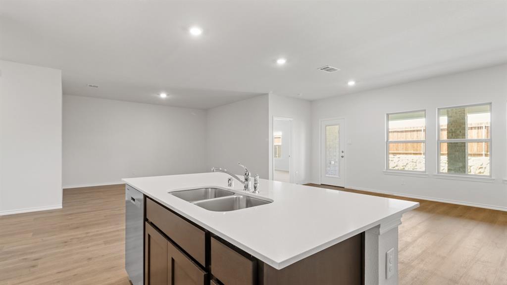 1923 Reveille Way Terrell, TX 75160 - Photo 11 of 33 Kitchen island featuring a double-basin stainless steel sink, a chrome faucet, and integrated dishwasher, all topped with a white countertop