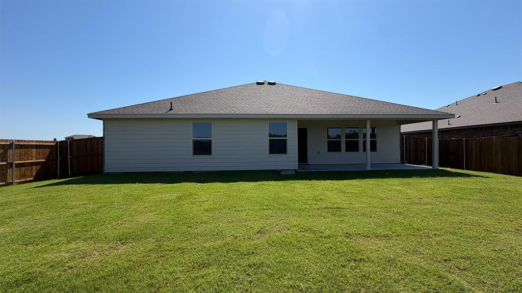 1923 Reveille Way Terrell, TX 75160 - Photo 28 of 33 Expansive backyard featuring a lush lawn, privacy fencing, a covered patio, and a single-story residence with a gray shingle roof