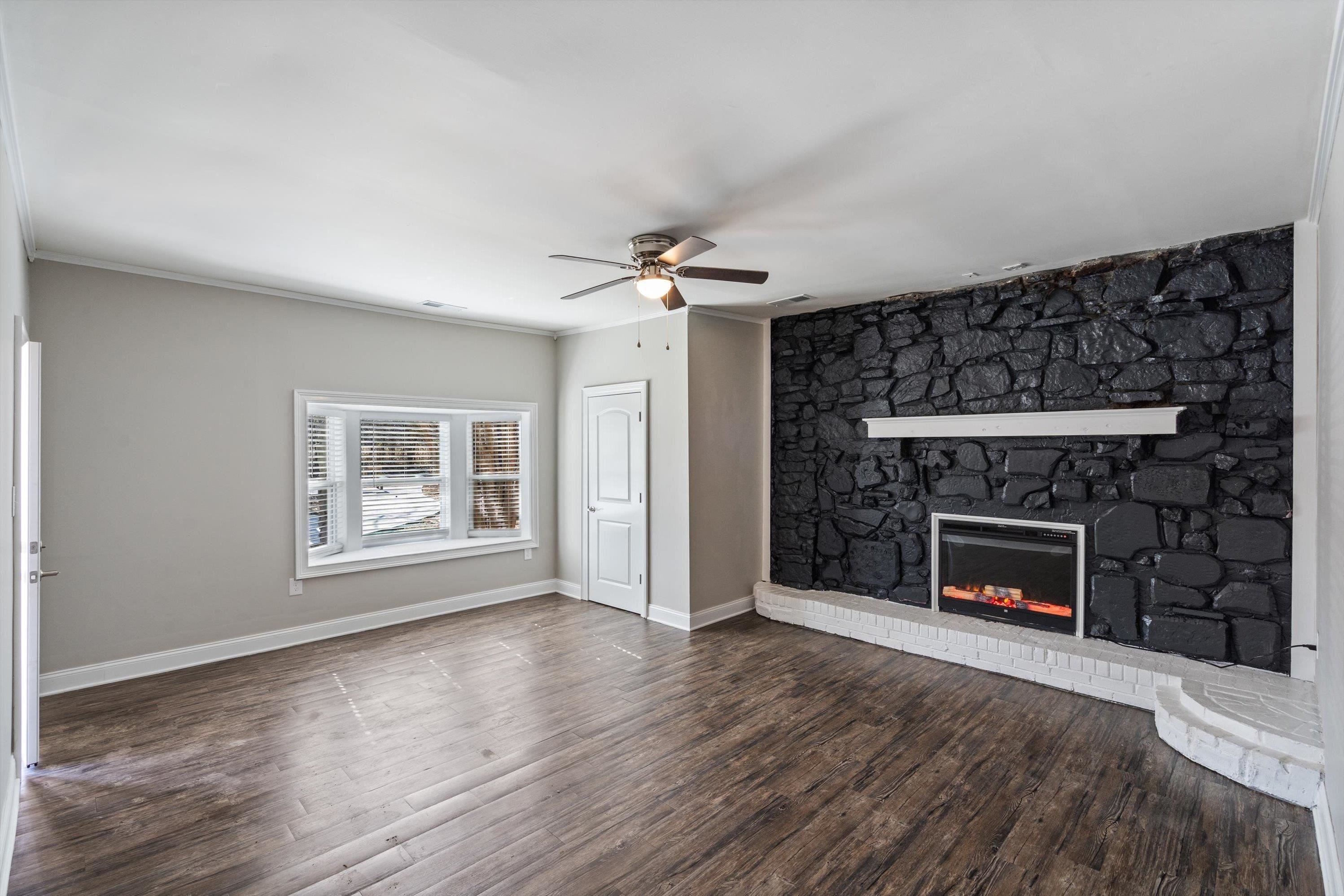 10464 East Holmes Road Collierville, TN 38017 - Photo 9 of 12 Unfurnished living room with dark wood-style floors, a fireplace, a ceiling fan, and crown molding