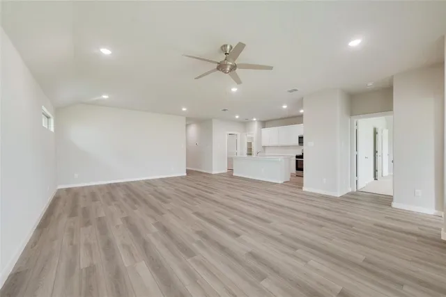 a view of an empty room with wooden floor and a ceiling fan