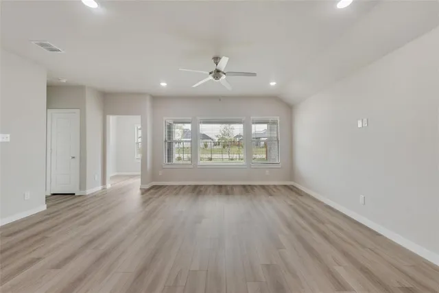an empty room with wooden floor chandelier fan and windows