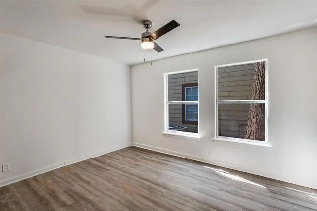 an empty room with wooden floor chandelier fan and windows