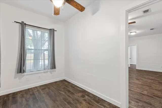 an empty room with wooden floor chandelier fan and windows
