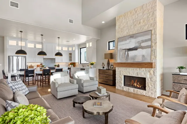 a living room with couches a fireplace and kitchen view with wooden floor