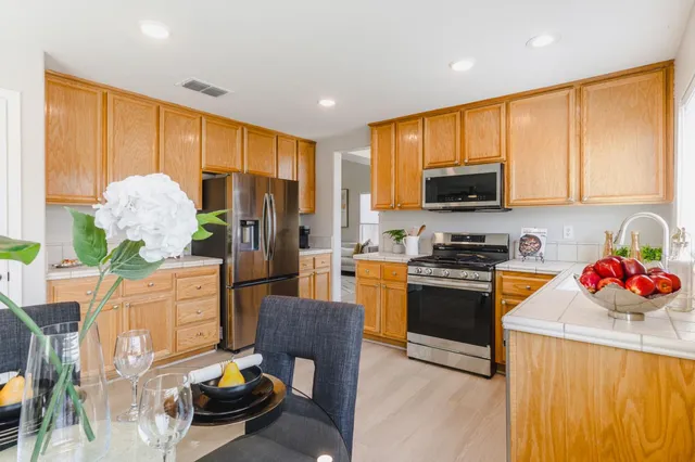 a kitchen with stainless steel appliances granite countertop a refrigerator a sink dishwasher a dining table and chairs with wooden floor