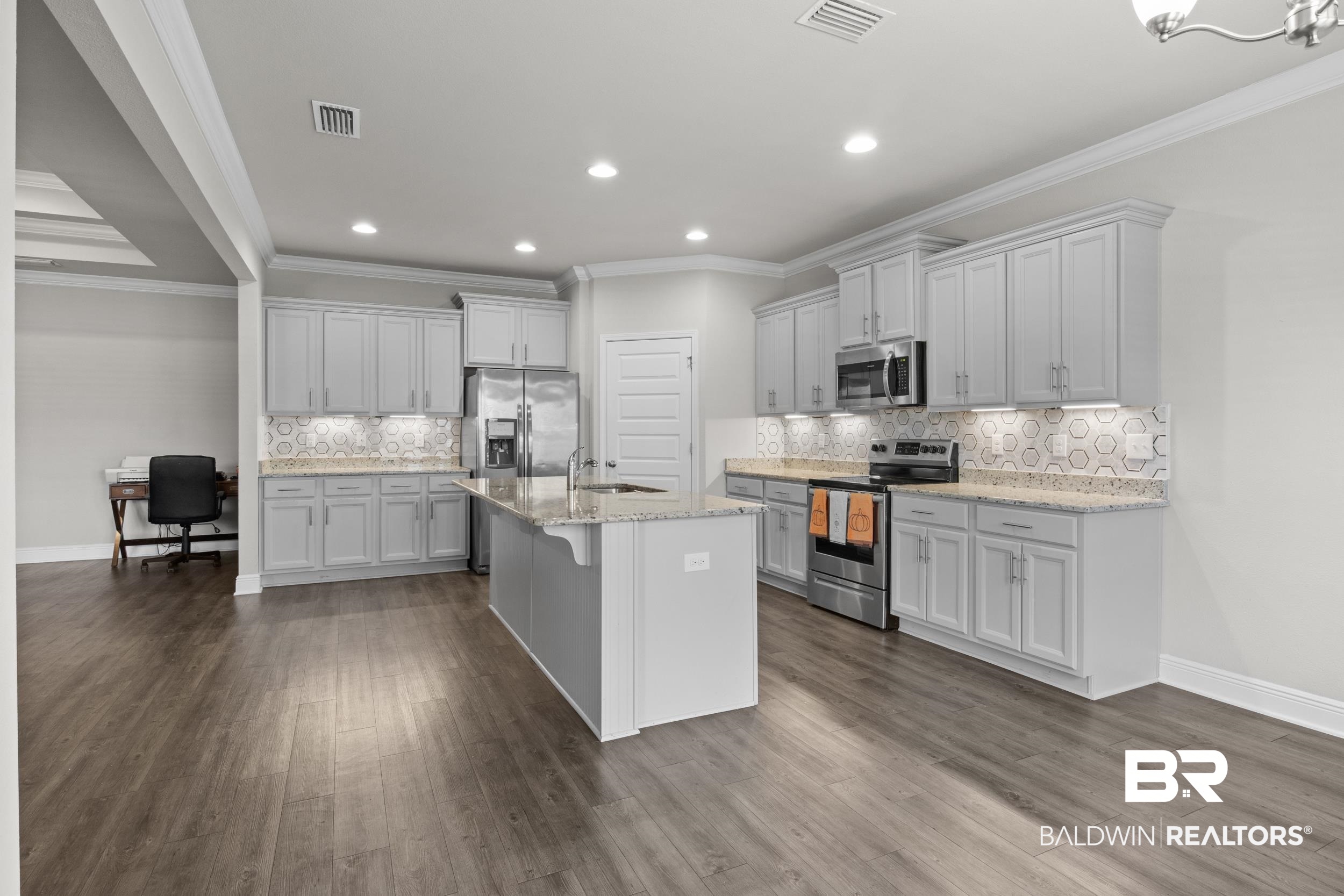 2050 Bourbon Street Foley, AL 36535 - Photo 14 of 32 Kitchen featuring light stone counters, stainless steel appliances, crown molding, a center island with sink, and dark hardwood / wood-style floors