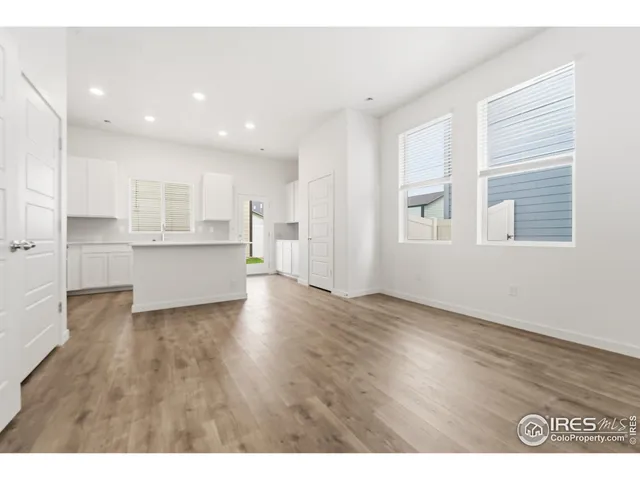 a view of an empty room with wooden floor and kitchen