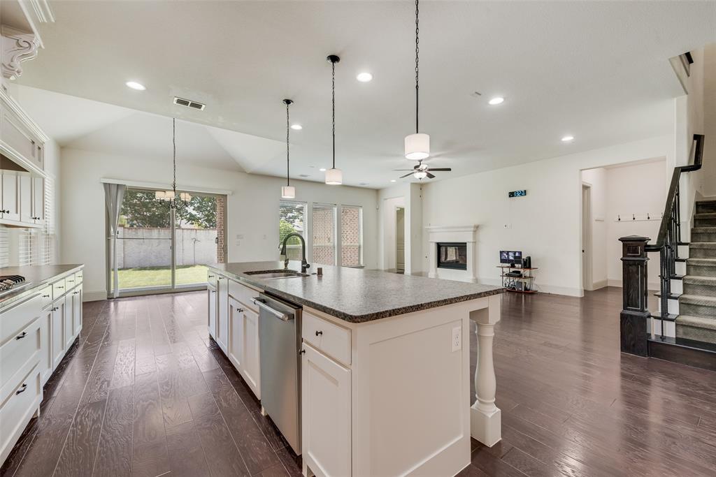 2021 Calisto Way Allen, TX 75013 - Photo 16 of 34 Open-concept living area featuring dark wood-finish flooring, a kitchen island with granite-style countertop, white cabinetry with dark hardware, a built-in fireplace, and a staircase with dark wood newel post and railings