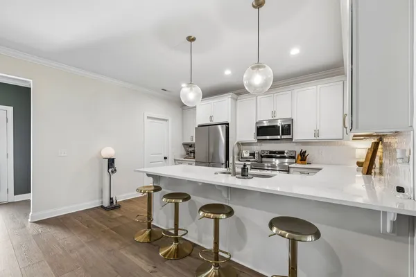 a kitchen with stainless steel appliances granite countertop a sink a stove a refrigerator and chairs with wooden floor