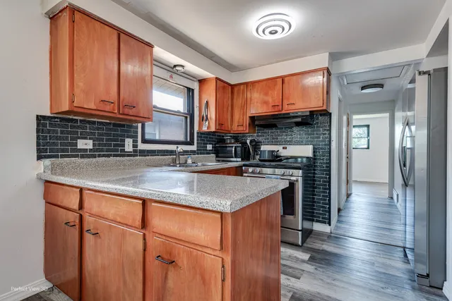 a kitchen with stainless steel appliances granite countertop a stove a sink and a refrigerator with wooden floors