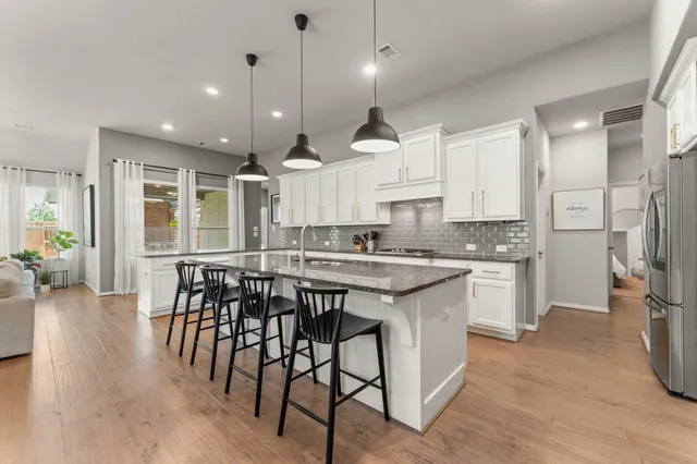 a kitchen with stainless steel appliances kitchen island granite countertop a stove a sink a refrigerator and a dining table with wooden floor