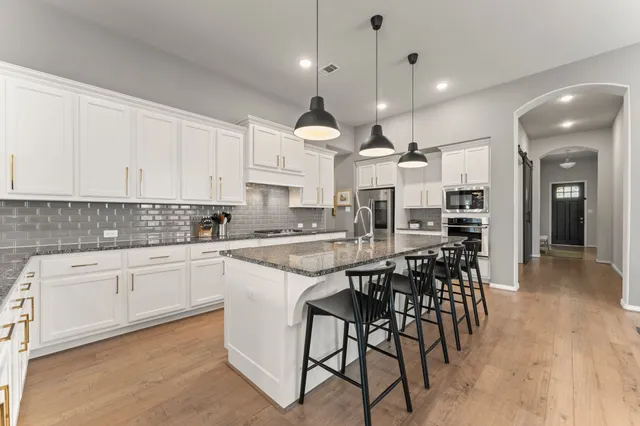 a kitchen with stainless steel appliances kitchen island granite countertop a dining table chairs sink and cabinets