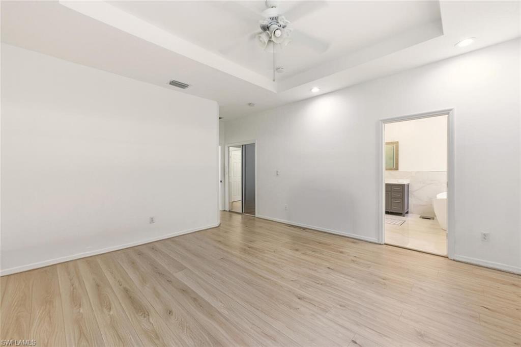 14978 Summit Pl Circle Naples, FL 34119 - Photo 16 of 35 Empty room featuring a tray ceiling, light wood-style floors, a ceiling fan, and recessed lighting