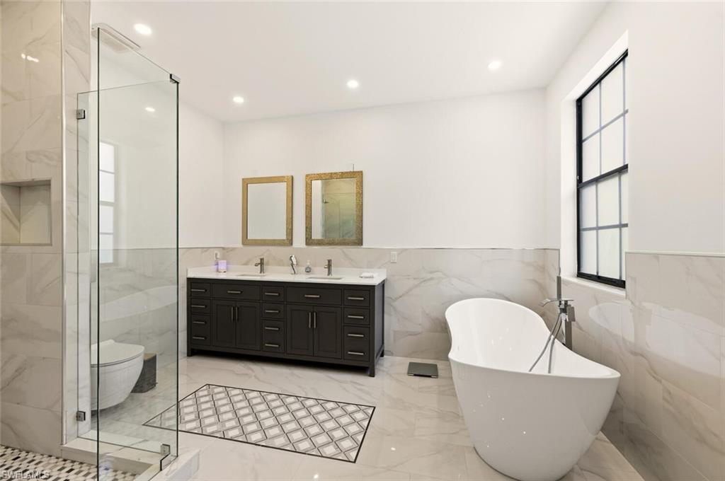14978 Summit Pl Circle Naples, FL 34119 - Photo 17 of 35 Bathroom with a soaking tub, light marble finish floors, tile walls, double vanity, and recessed lighting