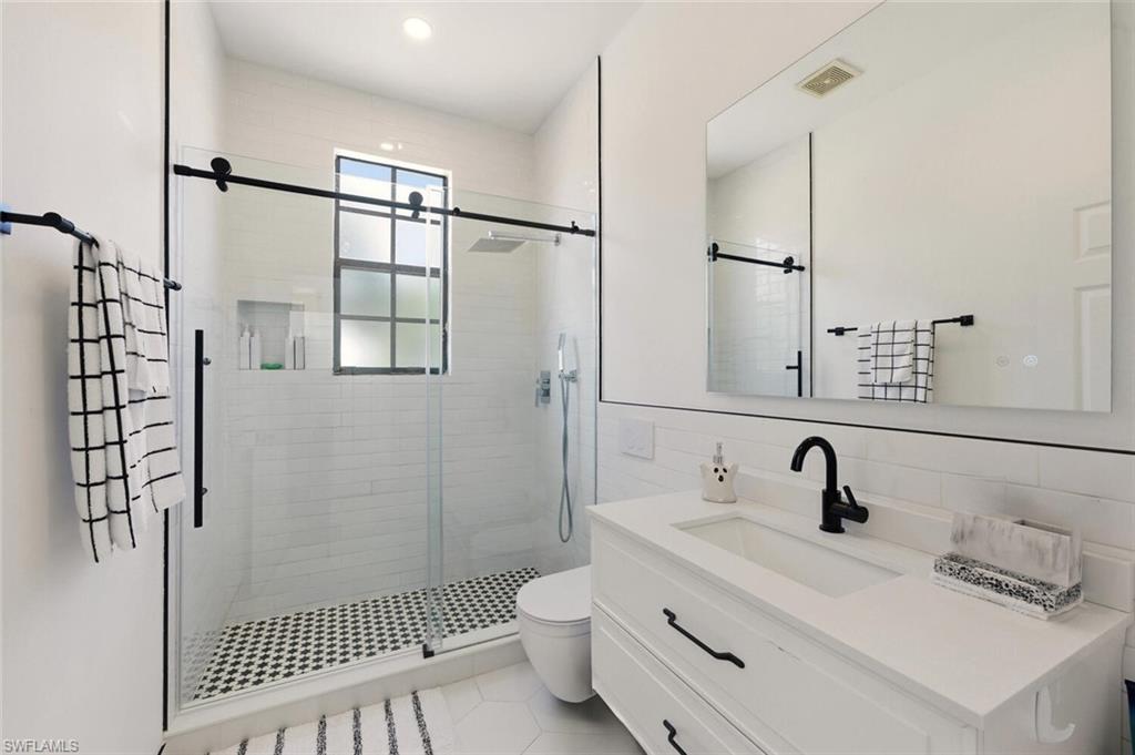 14978 Summit Pl Circle Naples, FL 34119 - Photo 21 of 35 Bathroom featuring vanity, a stall shower, tile walls, light tile patterned flooring, and tasteful backsplash