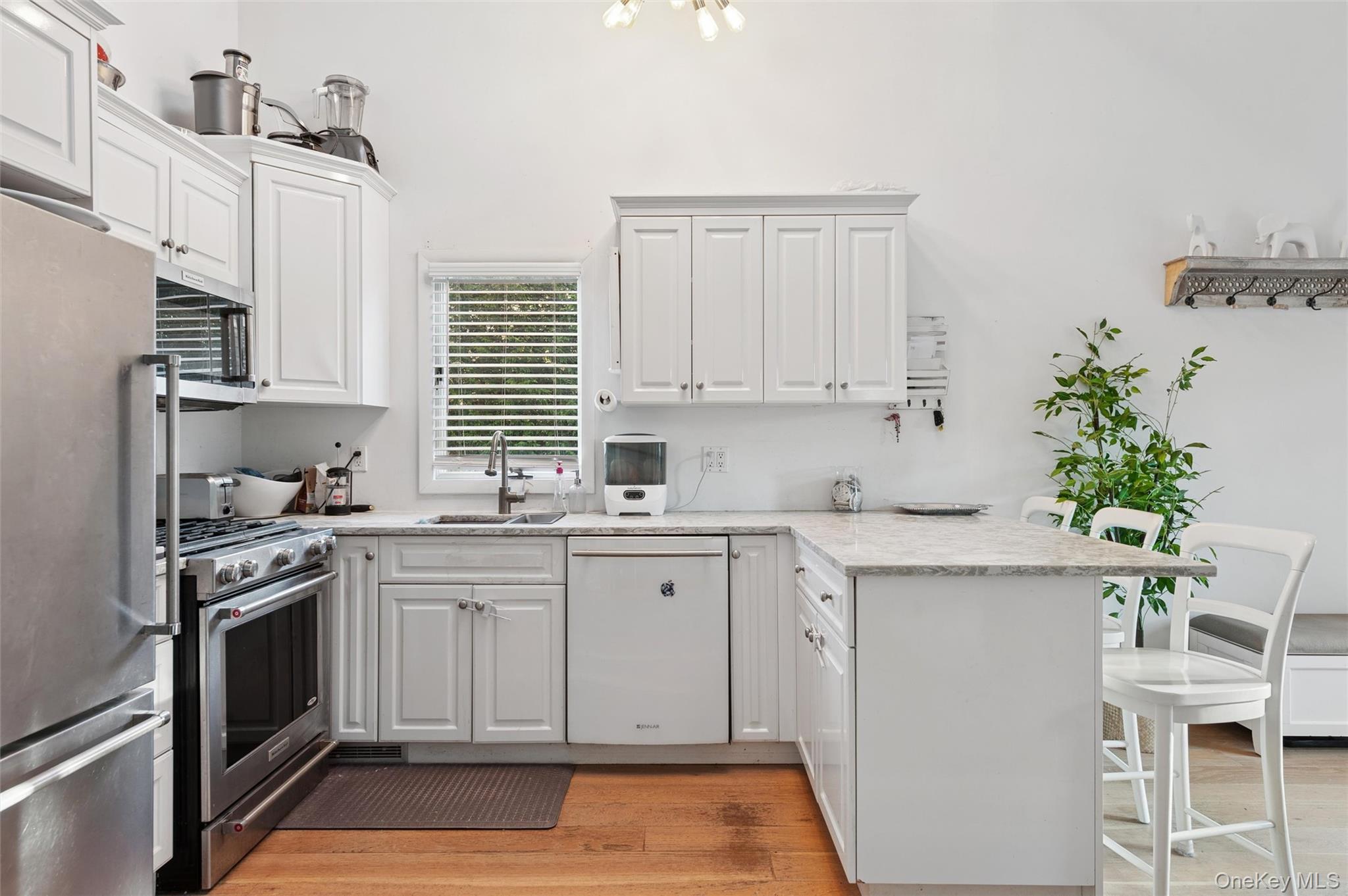 6 Shore Road Southampton, NY 11968 - Photo 4 of 15 Kitchen with a peninsula, appliances with stainless steel finishes, white cabinets, a breakfast bar, and light wood-type flooring