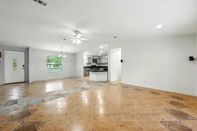 a view of an empty room with kitchen and window