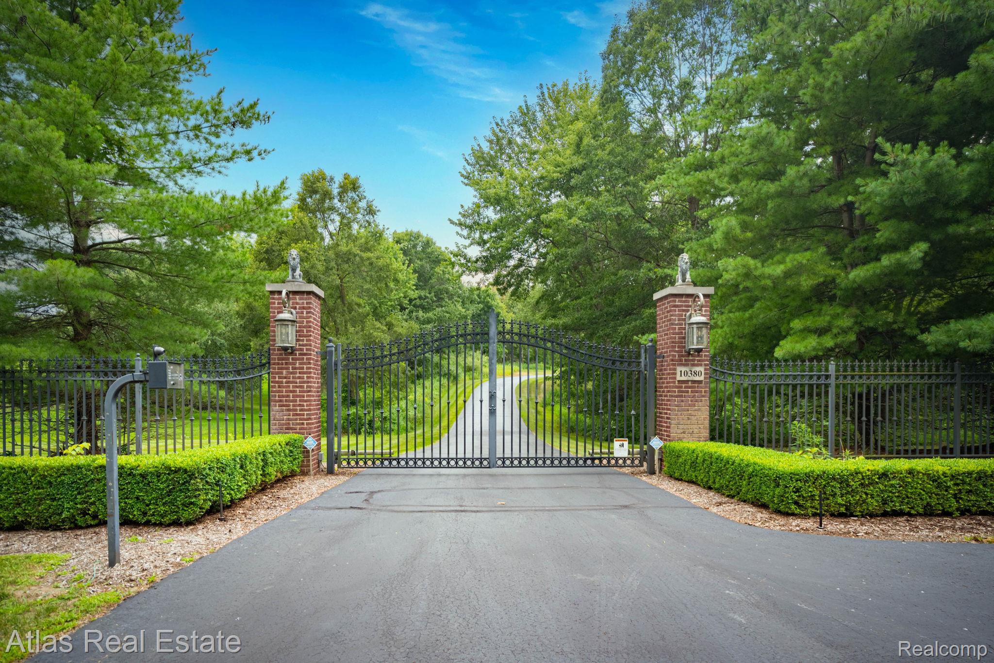 10380 South State Road Goodrich, MI 48438 - Photo 3 of 87 Gated entry featuring brick pillars with decorative finials, wrought iron fencing, and a paved driveway bordered by manicured hedges