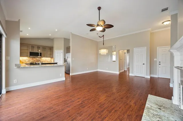 a view of an empty room and kitchen with wooden floor