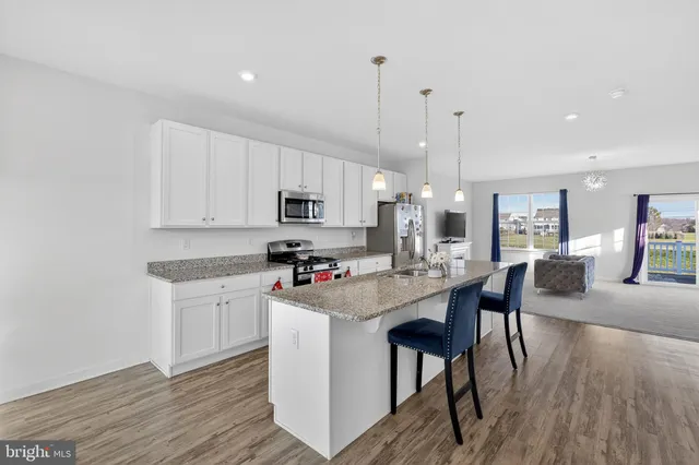 a kitchen with stainless steel appliances kitchen island granite countertop a stove a sink a refrigerator and white cabinets with wooden floor