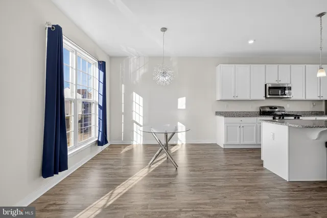 a kitchen with stainless steel appliances kitchen island granite countertop a refrigerator a stove a microwave oven a dining table and chairs with wooden floor