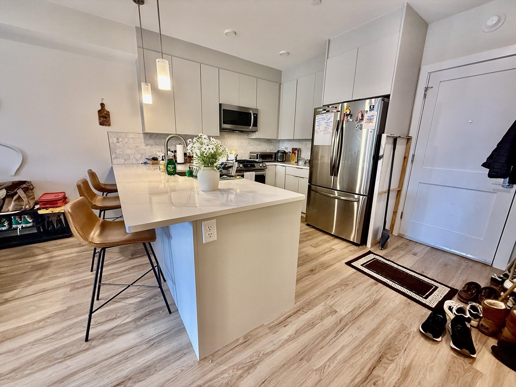 458 Washington Street, Unit 308 Boston, MA 02135 - Photo 3 of 14 a kitchen with stainless steel appliances a refrigerator a stove a sink dishwasher and a dining table with wooden floor