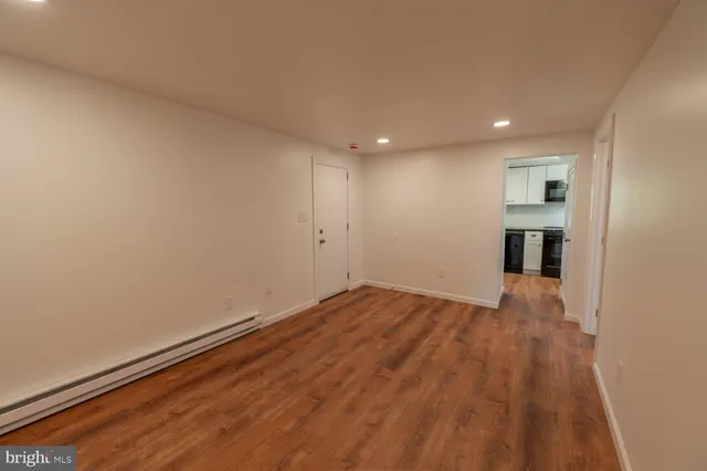 a view of empty room with wooden floor and kitchen