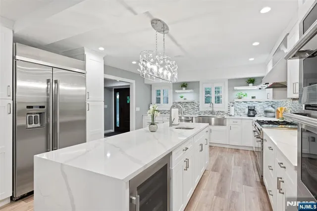 a large white kitchen with cabinets a counter top space stainless steel appliances and a chandelier